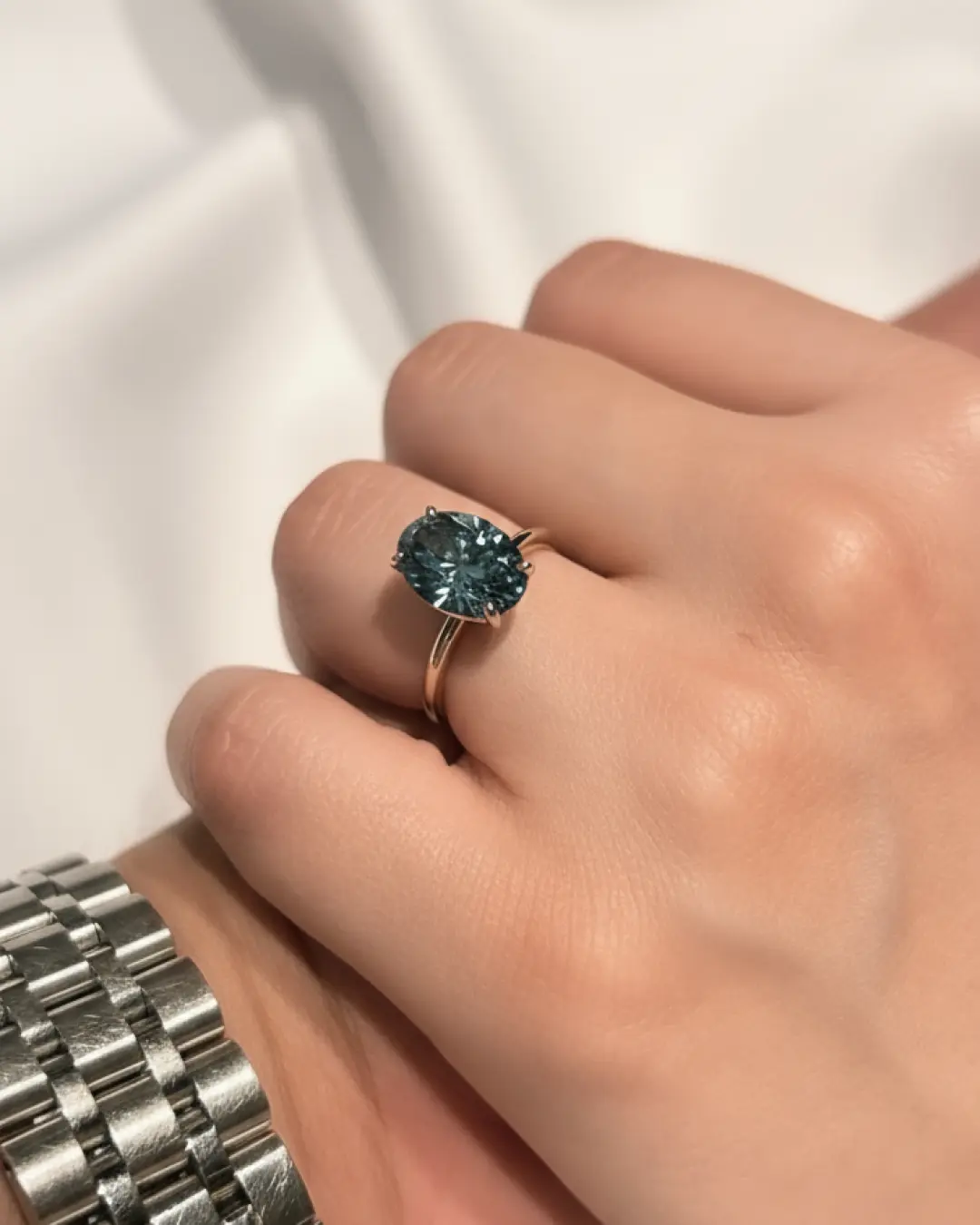 A hand wearing a custom oval teal sapphire solitaire ring in a gold band
