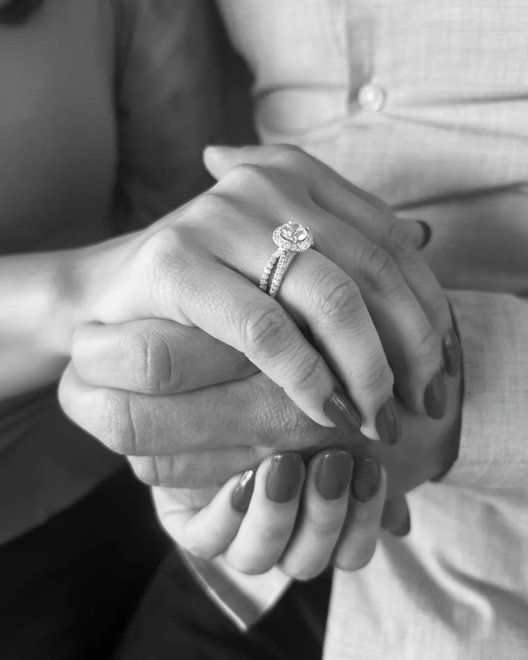 A couple holding hands, the bride-to-be wearing a custom diamond halo engagement ring, in black and white